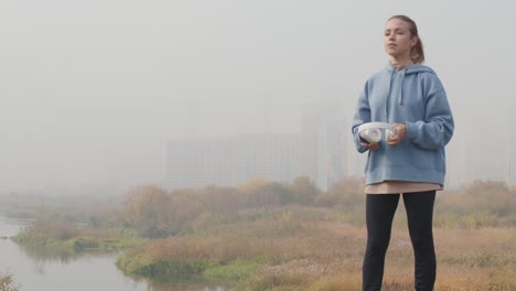 Young-Serious-Sportswoman-In-Blue-Hoodie-Putting-On-Headphones-And-Looking-At-The-Horizon-In-The-Woods-On-A-Cloudy-Day