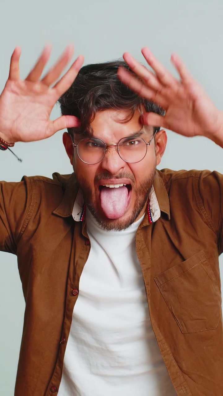 Cheerful funny bully indian man showing tongue making silly faces fooling around joking teasing