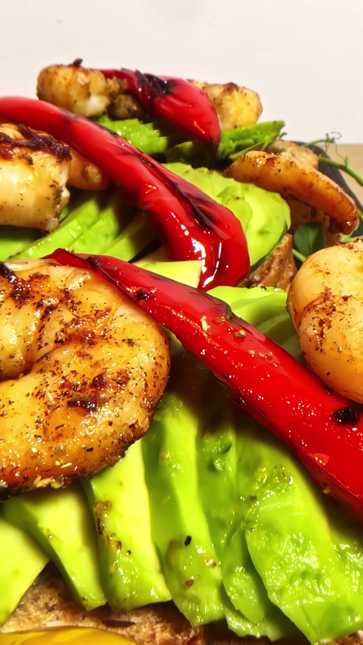Gamberi grigliati succosi e peperoni rossi carbonizzati disposti su avocado fresco a fette e pane tostato integrale, che mostrano un pasto vivace e sano. Video verticale, ideale per i social media.