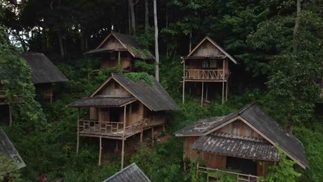 Revealing-shot-drone-moving-backwards-of-old-style-wooden-bungalow-resort-that-are-now-derelict-and-unused-due-to-the-effects-of-the-pandemic-on-travel-and-tourism