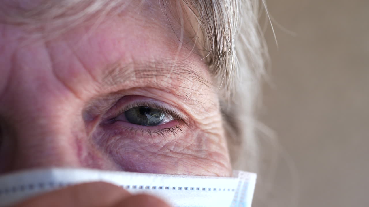 Primo piano del volto di un'anziana donna che indossa una mascherina per pazienti per prevenire la diffusione di una malattia contagiosa o evitare di ammalarsi