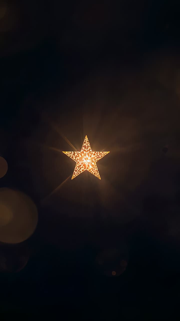 Vertical video: Zooming camera toward lit star lantern in dark room, showing pattern and warm bokeh