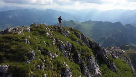 Drone-flying-backwards-while-a-young,-fit-man-is-running-down-the-rocky-trail-on-the-edge-of-the-ridge