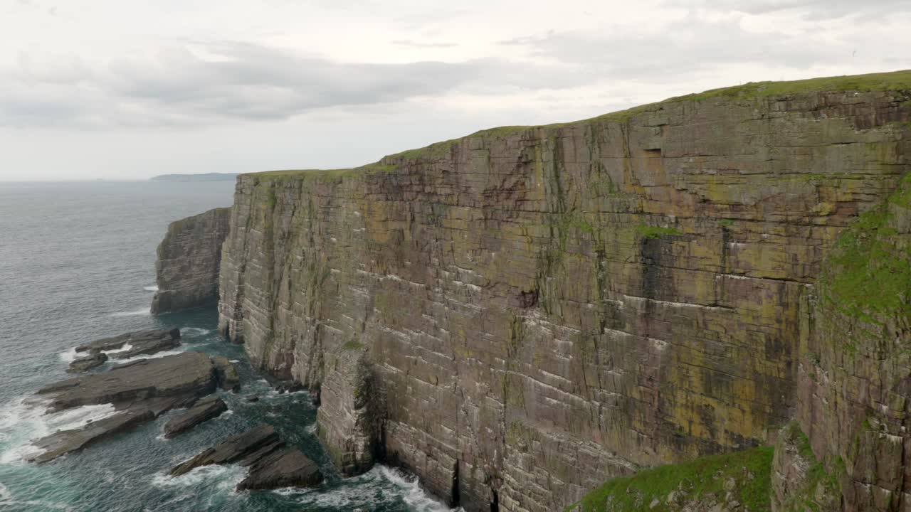 una toma panorámica lenta que revela aves marinas volando sobre un océano verde turquesa frente a un espectacular acantilado cubierto por una colonia de aves marinas con olas rompiendo contra su base
