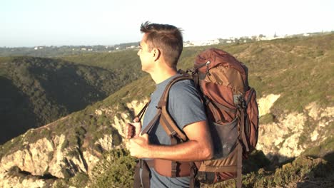 excited male backpacker standing at rocky cliff