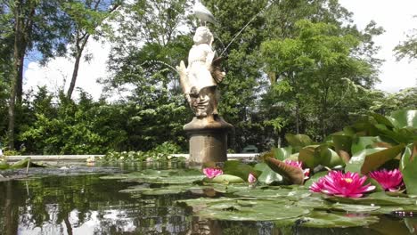 pink waterlilies floating on pond water with statue fountain at the rotterdam zoo in netherlands