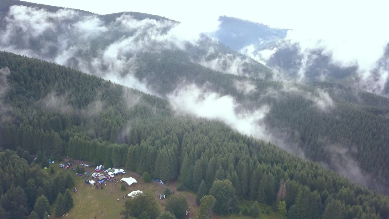 toma aérea de un drone de un campamento del festival golpeando para revelar la inmensidad de la ladera de la montaña de rumania cubierta por la niebla del valle temprano en la mañana.