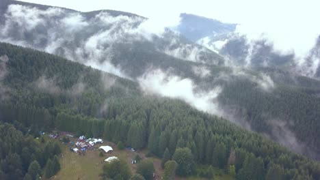 aerial drone shot of a festival campground punching in to reveal the vastness of the romania mountainside covered in early morning valley fog