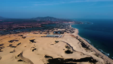 Coastal-yellow-sandy-dunes-with-city-in-horizon-in-Vietnam,-high-altitude-drone-view