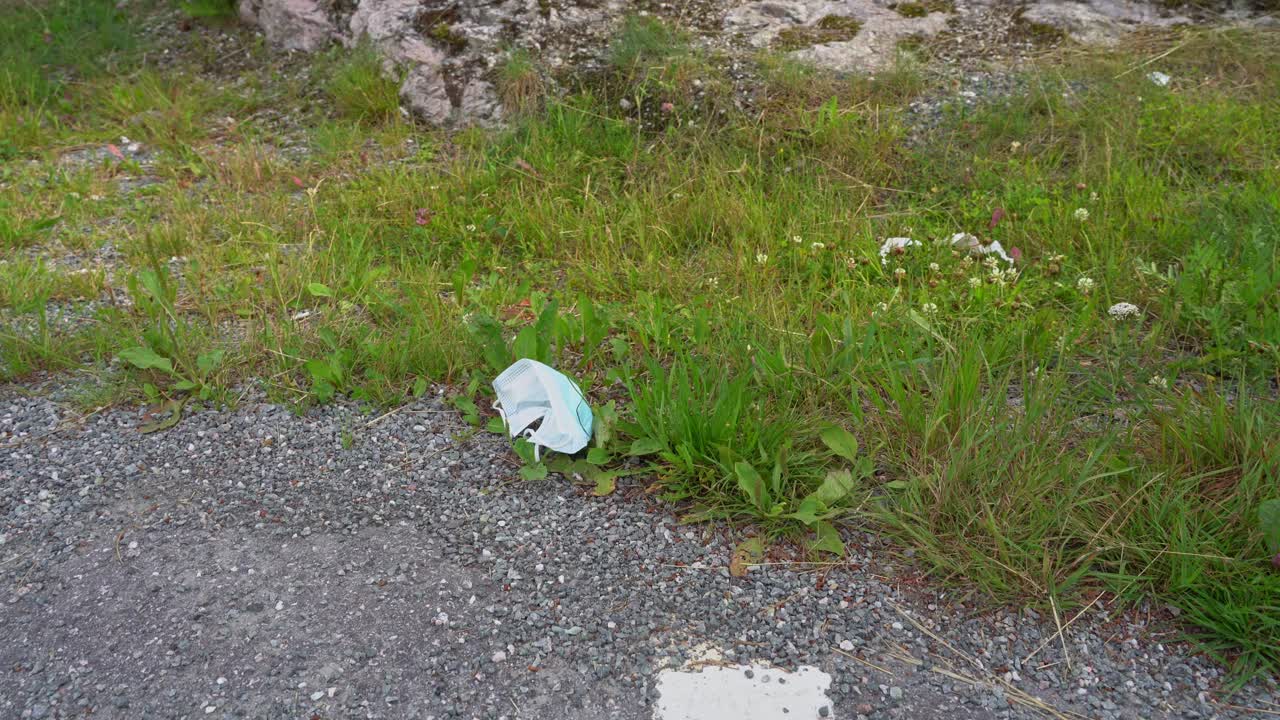 Used disposable facemask laying in green grass at roadside - littering problem
