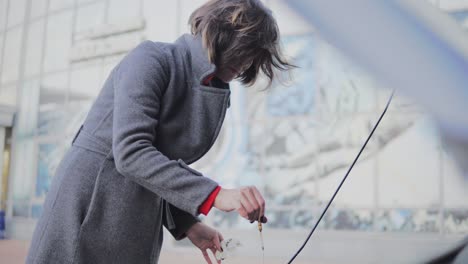 Business woman checks the oil level in the car looking under the hood in the street. Putting back the dipstick