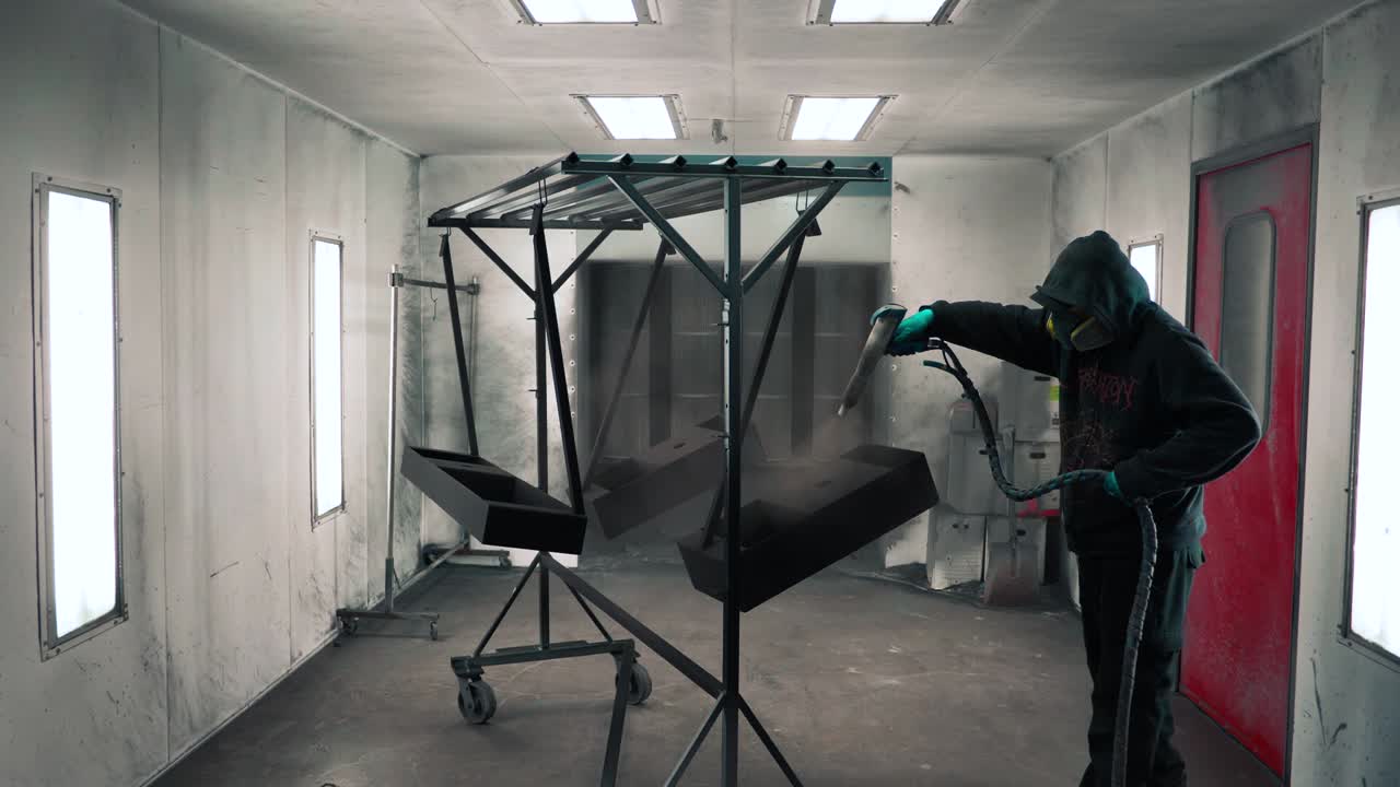 hombre que aplica un recubrimiento en polvo anticorrosión negro a una chapa metálica utilizando una pistola pulverizadora en la fábrica