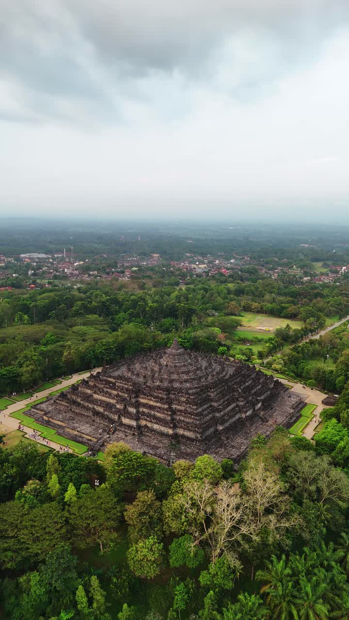 Sunset aerial of Borobudur, Central Java; stone stupas amid lush gardens, gentle right vertical drone orbit
