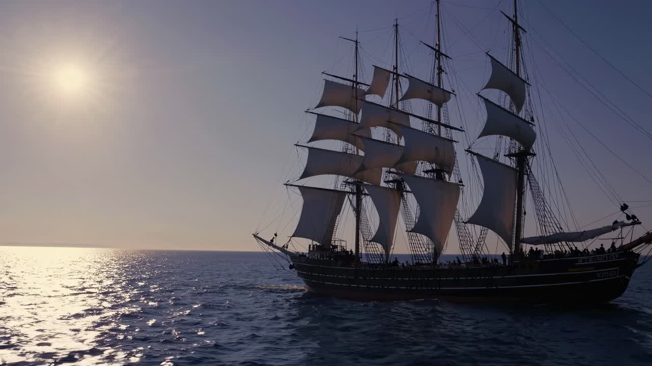 A majestic sailing ship glides on the ocean at sunset, captured from a low-angle in a cinematic