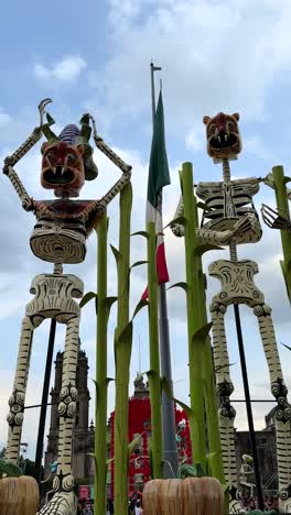 giant mexican skeleton sculptures adorn downtown with flag behind. zocalo, cdmx