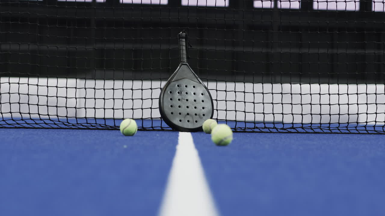 Padel racket and balls on indoor court near net, ready for match, copy space