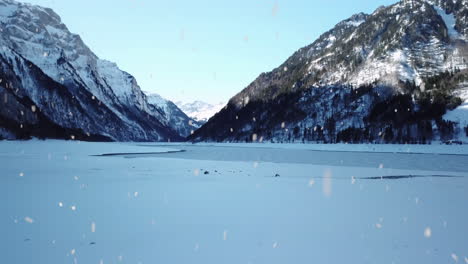 Winter-mountains-and-frozen-lake-surface-during-snowfall,-aerial-fly-forward-view