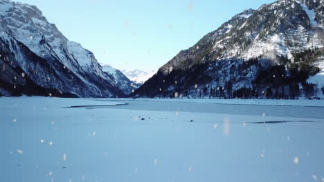 winter mountains and frozen lake surface during snowfall, aerial fly forward view