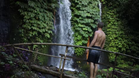 Slow-Motion-Shot-of-a-man-walking-in-front-of-one-of-the-many-beautiful-Banyu-Wana-Amertha-Waterfalls-in-the-jungles-of-Bali,-Indonesia