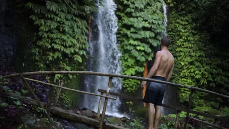 slow motion shot of a man walking in front of one of the many beautiful banyu wana amertha waterfalls in the jungles of bali, indonesia