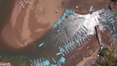 overhead drone shot of beach with fisherman boats docked on the harbor