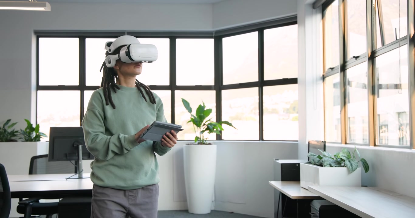 Personne africaine non-binaire avec un casque de réalité virtuelle blanc, haut couleur menthe, regardant vers le haut, tapotant une tablette et testant la réalité virtuelle dans un bureau.
