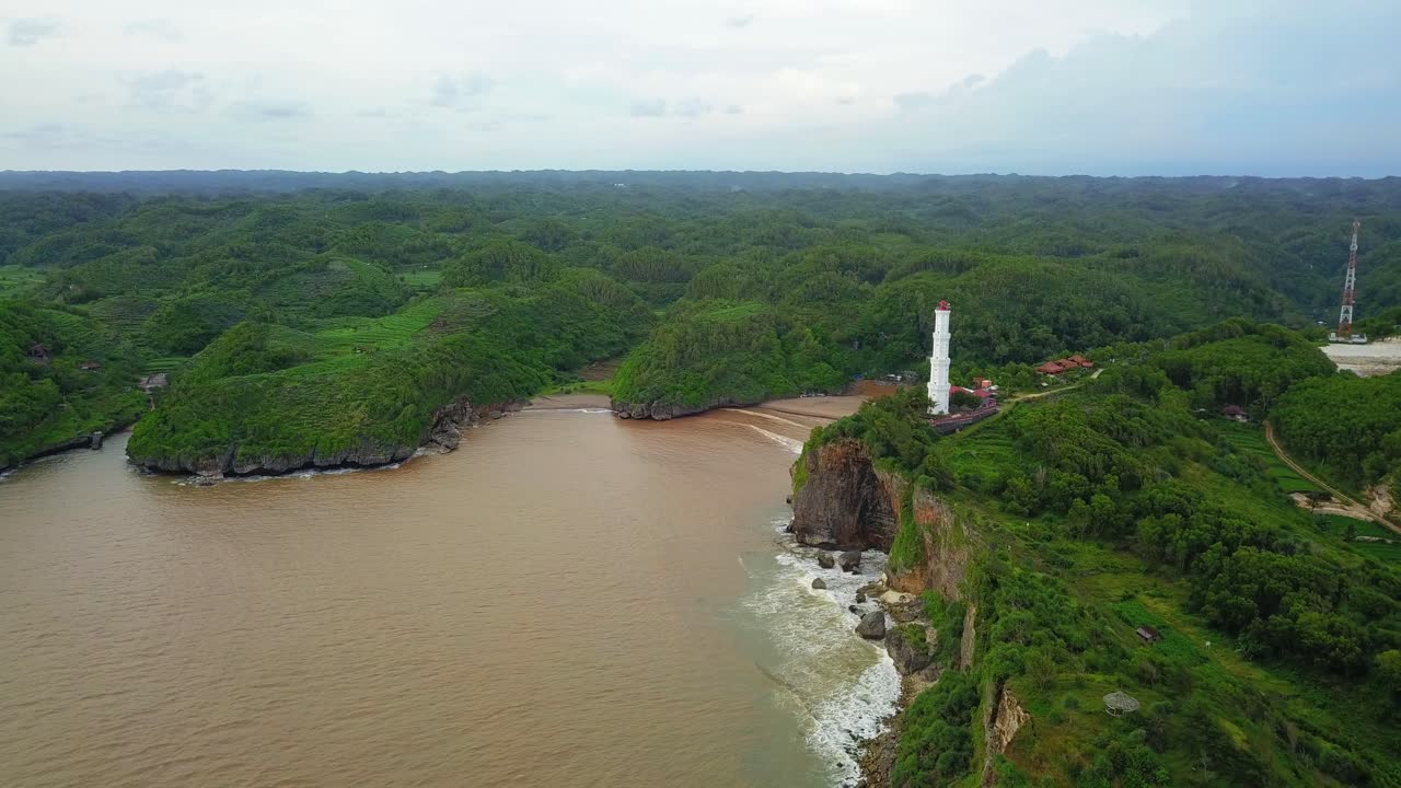 tiro de dron del faro blanco en la frontera de la colina con el océano