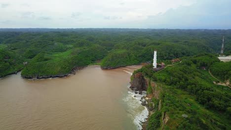Drone-shot-of-white-lighthouse-on-the-hill-border-with-ocean