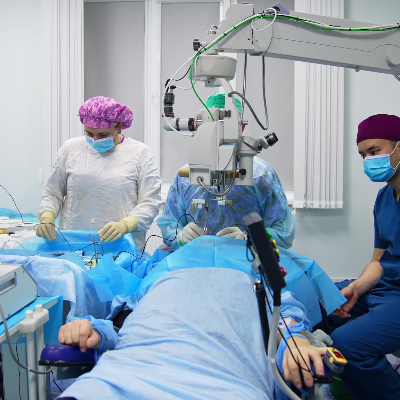 Patient lies under the technological equipment in surgery room. Team of doctors perform eye operation in modern clinic