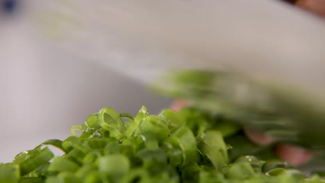 primer plano de cebollas verdes frescas siendo cortadas finamente en una tabla de cortar blanca