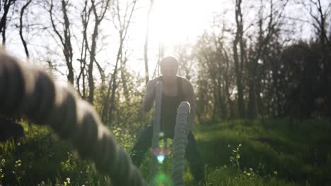 Muskulöser-Mann-Macht-Wellen-Mit-Crossfit-Seilen.-Bosk,-Sonnenstrahlen-Im-Hintergrund.-Vorderansicht,-Nahaufnahme-Der-Seile