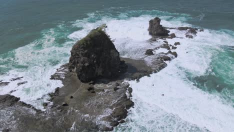 Aerial-view-of-coral-island-with-huge-towering-rock-in-ocean-tidal-waves