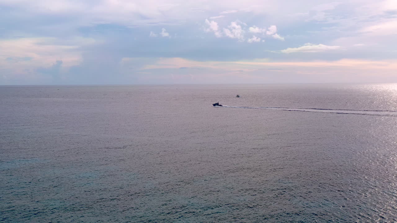 Aerial 4k shot of a motorboat sailing on a calm sea from right to left. Cloudy skies on the horizon.