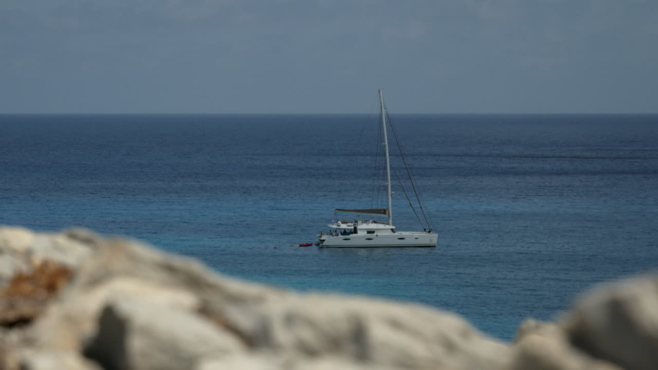 rocas de piedra borrosas y un velero blanco en el fondo del océano acuático en un día soleado en mallorca españa