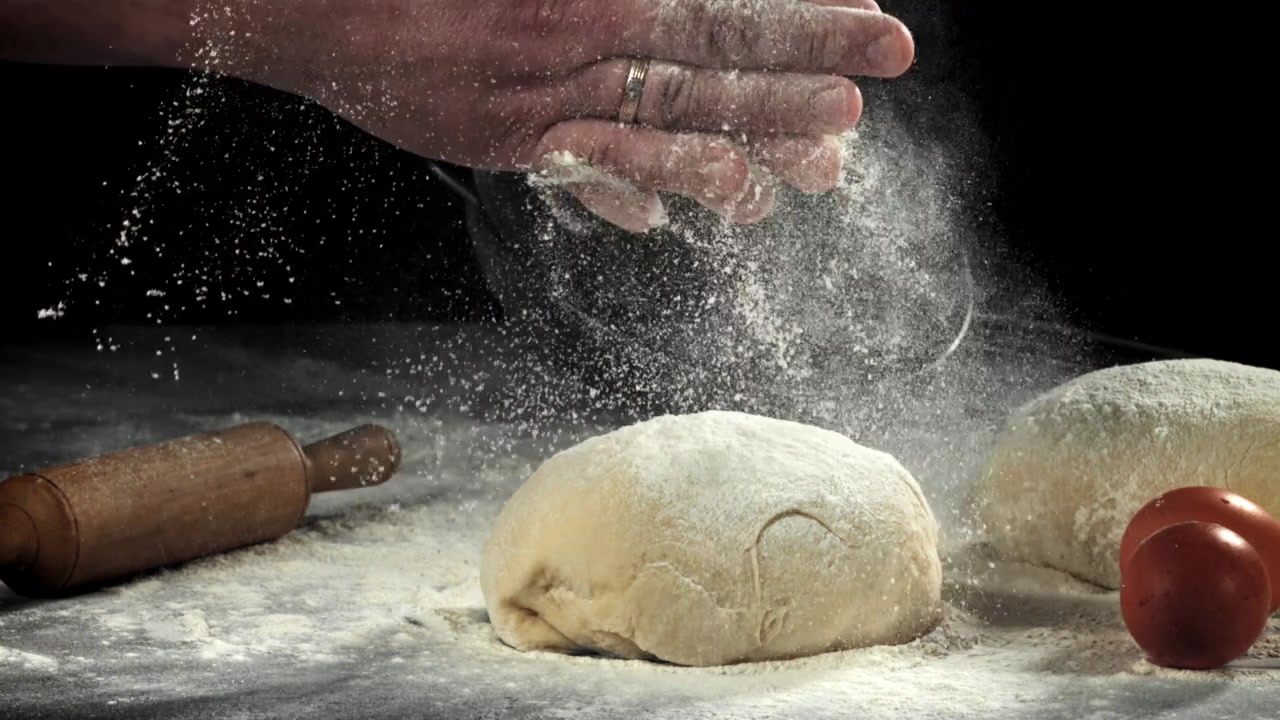 Primo piano di una mano che sparge farina su impasto crudo