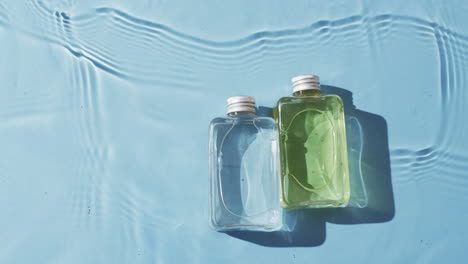 video of beauty product bottles in water with copy space on blue background