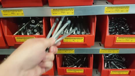 a human hand takes out five large bolts from a red storage bin in a steel industrial rack. close up