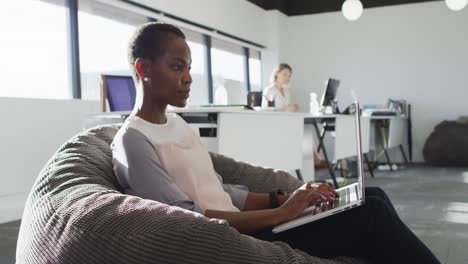 african american businesswoman sitting in armchair and using laptop