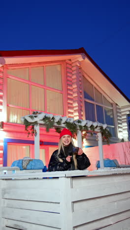 calm attractive caucasian woman wearing red cap and black coat stands outdoors. cheering smiling lady drinks tea at the porch. vertical video.