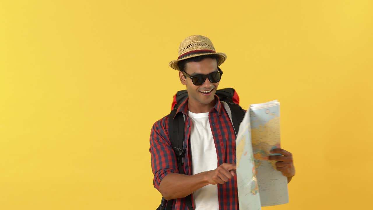 un mochilero asiático sonriente caminando y mirando el mapa