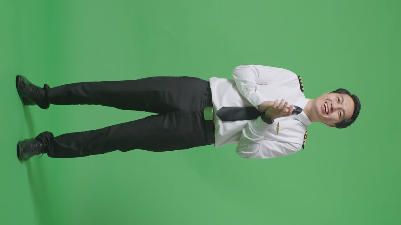 녹색 스크린 배경 스튜디오에 서 있는 동안 미소 짓고 손을 치는 아시아 남성 조종사의 몸이 가득 차 있습니다.