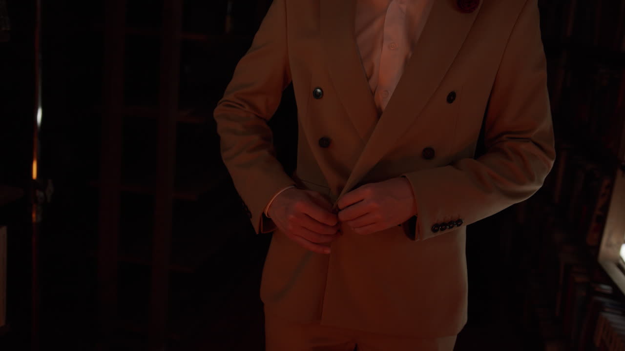 Man Buttoning Up a Light Brown Suit in a Library