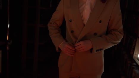 man buttoning up a light brown suit in a library