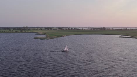 Wide-shot-of-sailing-vessel-exploring-Friesland-lake-during-sunset,-aerial