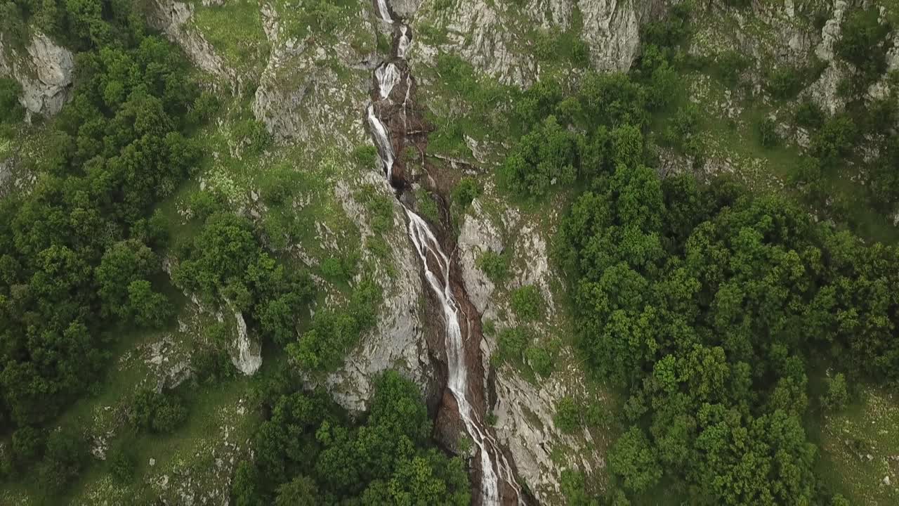 Aerial view of a landscape with a waterfall cascading down a rocky terrain surrounded by trees and greenery