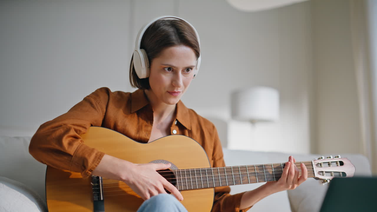 Woman studying guitar play watching laptop tutorial video in earphones closeup