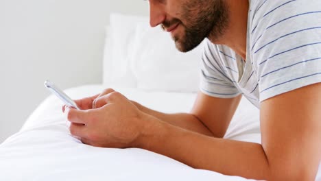 Hombre-Sonriente-Usando-Un-Teléfono-Móvil-En-La-Cama-En-El-Dormitorio