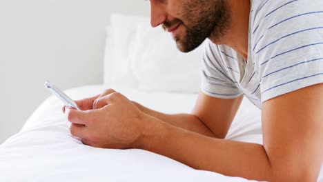 hombre sonriente usando teléfono móvil en la cama en el dormitorio