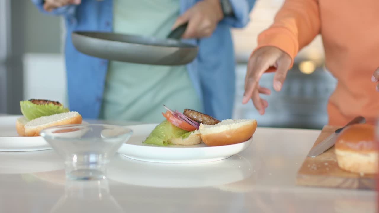 Dopo aver preparato un hamburger, diversi amici si riuniscono attorno al bancone della cucina per assemblare l'hamburger per pranzo