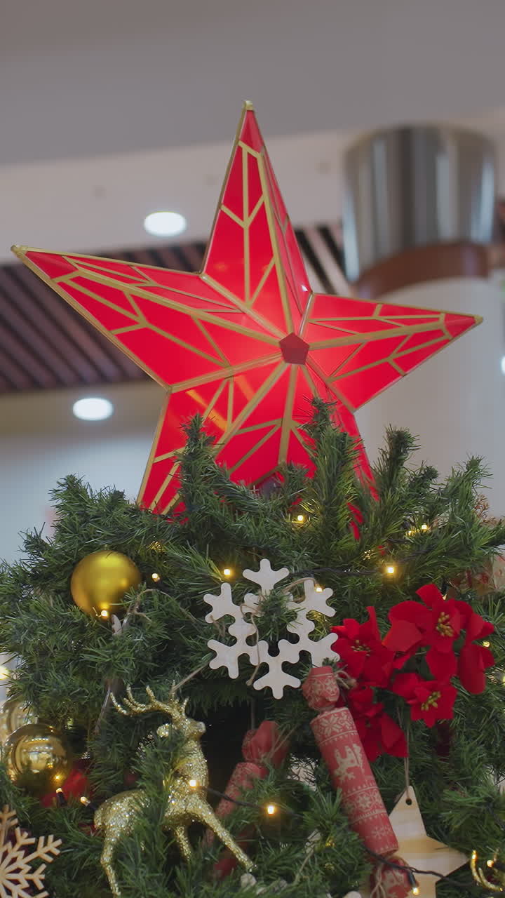 Close-up of beautifully decorated Christmas tree with glowing red star topper, golden ornaments, snowflakes, and festive decorations adorn lush green branches